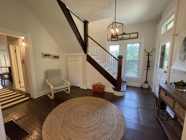 A spacious living room with a wooden staircase, a round woven rug, and a dining area with a striped rug.