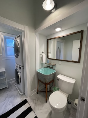 A bathroom with a washing machine, a sink, a toilet, and a mirror.