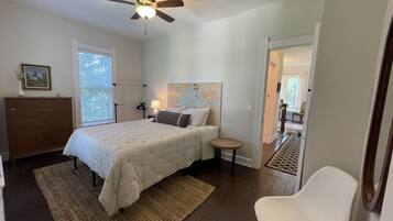 Une chambre à coucher comprenant un lit, des tables de chevet, un ventilateur de plafond, une commode et une chaise.