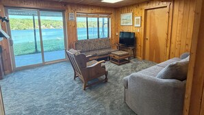 A cabin interior with a sofa, wooden furniture, a television, and a view of a lake through large windows. - 4 Bedroom Lake House - Northern Michigan (Central Lake)