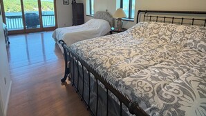 A bedroom with a large bed, a ceiling fan, and a view of a balcony with a grill. - 4 Bedroom Lake House - Northern Michigan (Central Lake)