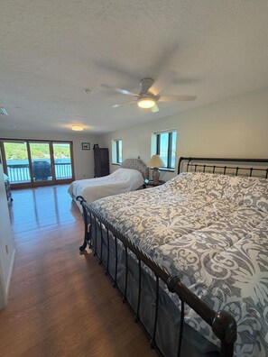 A bedroom with a large bed, a ceiling fan, and a view of a balcony with a grill. - 4 Bedroom Lake House - Northern Michigan (Central Lake)