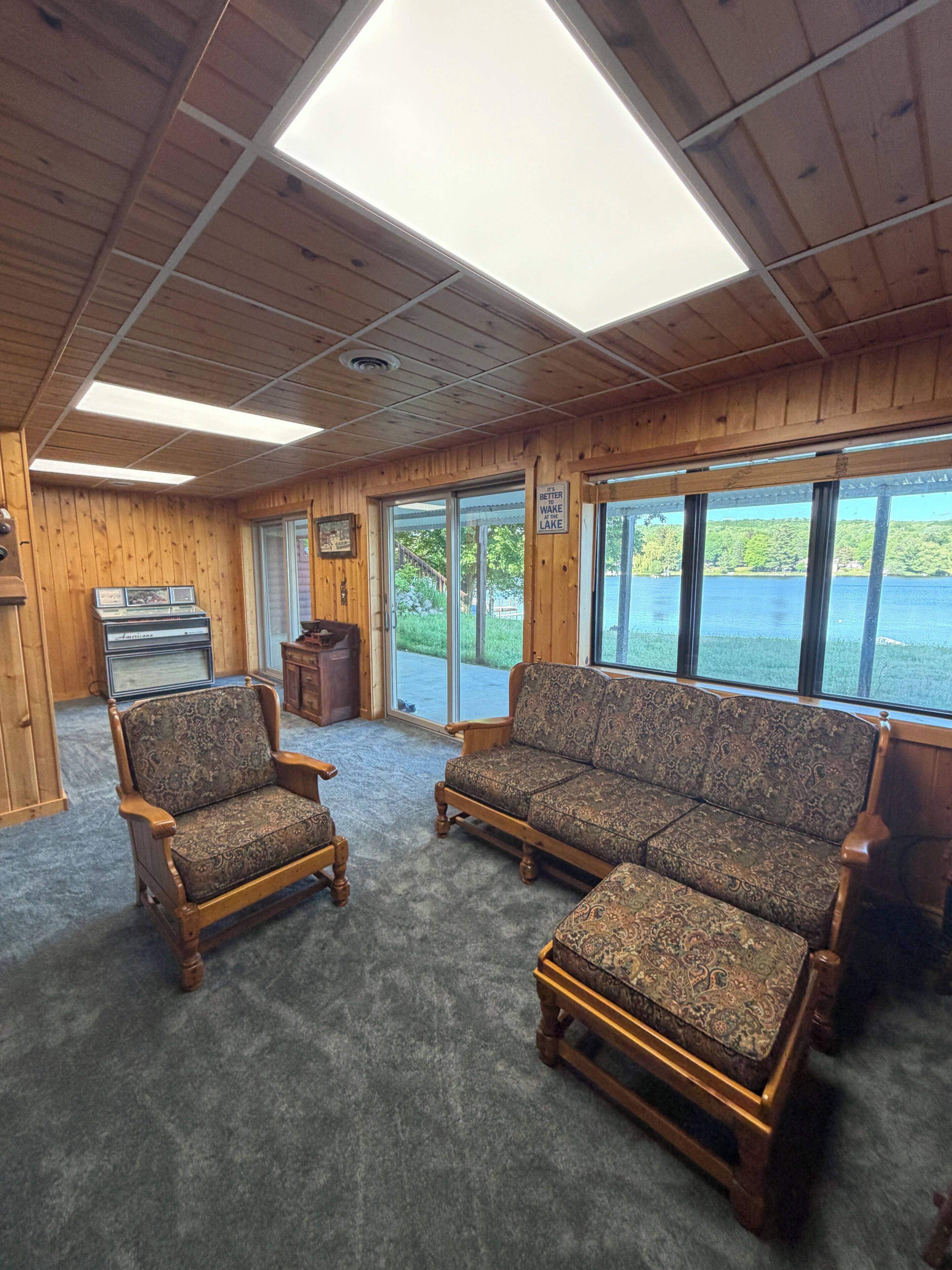 Eine Holzhütte mit einer Couch, einem Sessel, einem Klavier und einem großen Fenster mit Seeblick.