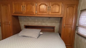 A bedroom with a bed, wooden headboard, and built-in wooden cabinets. - Cozy RV in a vacation community on Lake Hartwell (Westminster)
