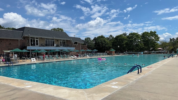 A swimming pool with lounge chairs and umbrellas, a brick building with a balcony, and a clear blue sky. - Cozy RV in a vacation community on Lake Hartwell (Westminster)