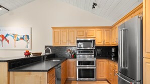 A modern kitchen with wooden cabinets, stainless steel appliances, and a black countertop. - RMR: Teton Pines 3443 Townhome in Wilson, WY (Wilson)