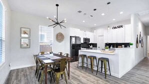 A modern kitchen with white cabinetry, a central island with stools, and a dining area with a wooden table and chairs. - Family Friendly | Patio | Fireplace | BBQ | Games (San Antonio)