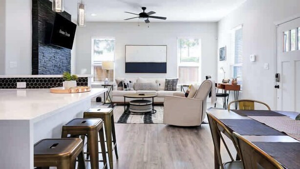 A modern kitchen with a white countertop, bar stools, and a dining area with a table and chairs. - Family Friendly | Patio | Fireplace | BBQ | Games (San Antonio)