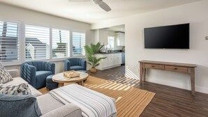Un salon moderne comprenant un canapé, des fauteuils, une table basse, un téléviseur et un ventilateur de plafond.
