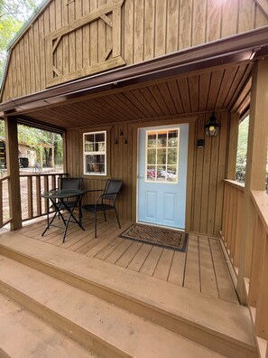 A wooden porch with a blue door, two windows, and a small table with chairs.