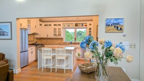 A modern kitchen with white cabinets, a central island, and a dining area with chairs. - Blackberry Meadow (New Shoreham)