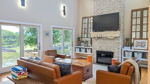 A spacious living room with a fireplace, leather sofas, and a television mounted on a brick wall. - Blackberry Meadow (New Shoreham)