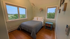 A bedroom with a bed, two windows, a heater, and a small table with a colorful design. - Blackberry Meadow (New Shoreham)