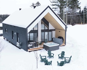 A modern cabin with a large deck, outdoor seating, and a hot tub.