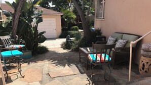 Una zona patio con pavimento in pietra, una sedia in vimini con un cuscino colorato, un divano in vimini con cuscini a fantasia e un tavolino.