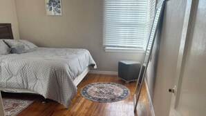 Una camera da letto con un letto, un poggiapiedi, un tappeto rotondo e una finestra con persiane.
