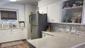 A modern kitchen with white cabinetry, a stainless steel refrigerator, and a marble countertop. - Paisley Dash House (Fargo)