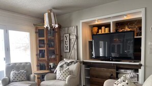 A cozy living room with a television, a wooden cabinet, and a large window. - Paisley Dash House (Fargo)