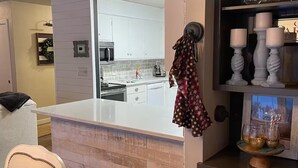 A modern kitchen with white cabinets, a wooden island, and a dining area with a chair. - Paisley Dash House (Fargo)