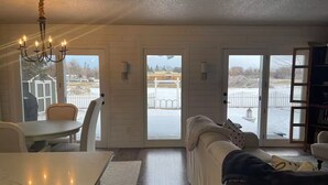 A cozy living room with a white couch, a dining table, and a chandelier. There are two sliding glass doors leading to a snowy outdoor area. - Paisley Dash House (Fargo)