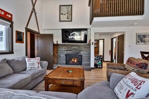 A modern living room with a stone fireplace, a flat-screen TV, and a sign for 'Ski Lodge at White Peak Mountain.' - Liquid Lodge: 6BR Multi-Family Hub with 3 Living Areas, Private Hot Tub & 4 PM Check Out (Killington)