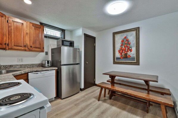 A kitchen with wooden cabinets, a stainless steel refrigerator, a microwave, a toaster, and a wooden bench. - Liquid Lodge: 6BR Multi-Family Hub with 3 Living Areas, Private Hot Tub & 4 PM Check Out (Killington)