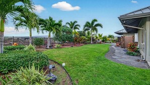 Een verzorgde tuin met palmbomen, een pad van natuursteen en een huis met een stenen gevel.