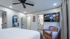 A hotel room with a bed, a chair, a ceiling fan, a TV mounted on the wall, and a door leading to another room. - Peaceful Rydal Retreat With Modern Comforts (Rydal)