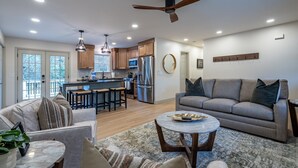 A spacious living area with a sofa, a coffee table, and a kitchen area with wooden cabinets and a refrigerator. - Peaceful Rydal Retreat With Modern Comforts (Rydal)