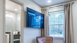A modern living room with a large flat-screen TV mounted on the wall, a plush armchair, a patterned rug, and a window with curtains. - Peaceful Rydal Retreat With Modern Comforts (Rydal)