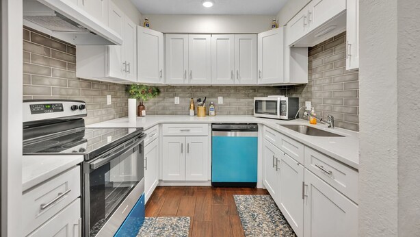 Une cuisine de taille réduite avec des meubles blancs, un lave-vaisselle bleu, un four à micro-ondes et une cuisinière.