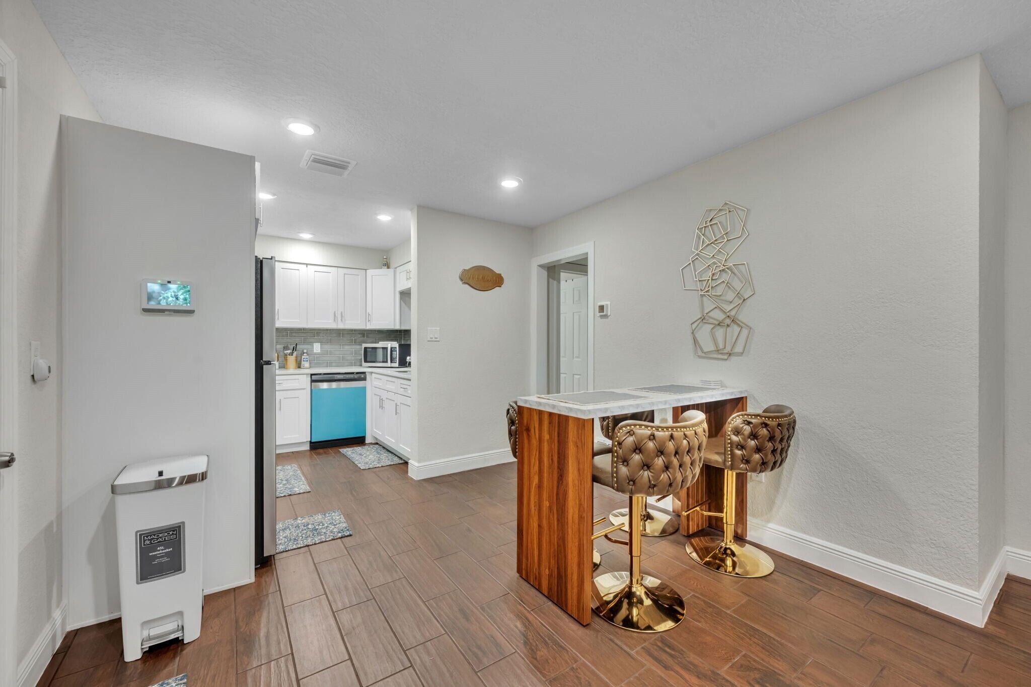 A modern kitchen with white cabinets, a blue countertop, and a wooden island. There are two gold bar stools with tufted leather seats.