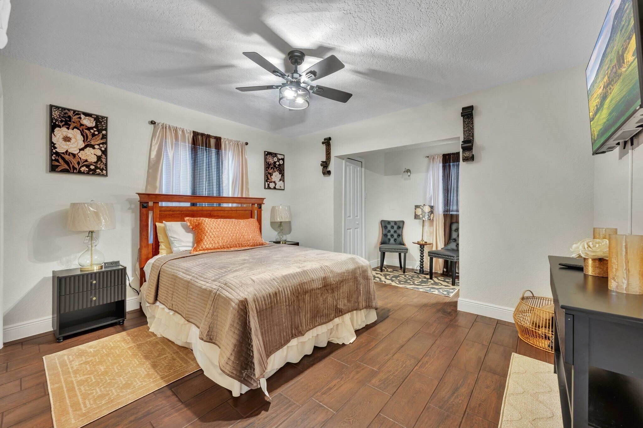 A bedroom with a bed, a ceiling fan, a nightstand, a lamp, a chair, and a desk.