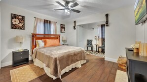 Une chambre à coucher comprenant un lit, un ventilateur de plafond, une table de chevet, une lampe, une chaise et un bureau.