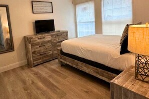 A bedroom with a wooden bed frame, a television on a dresser, and a lamp on a side table. - Houston Stay Near Downtown and Top Attractions (Houston)