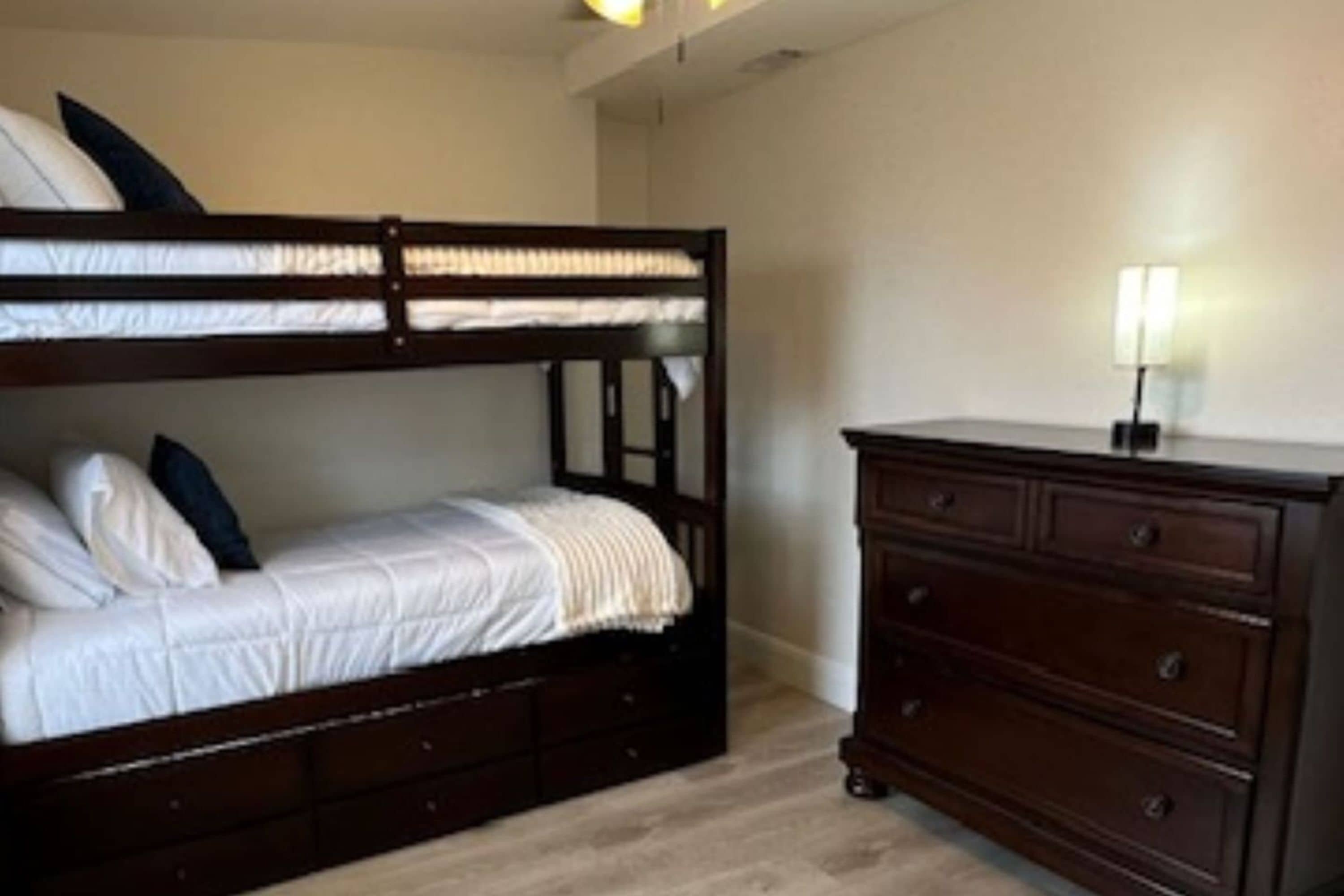 A bedroom with a bunk bed, a dresser, and a bedside lamp.
