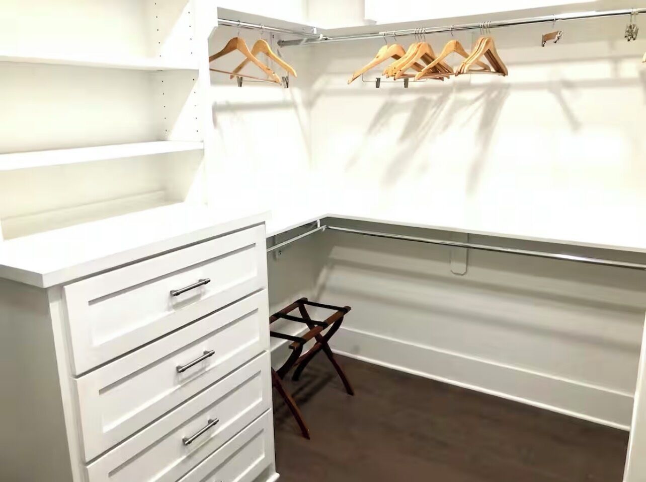 Ein begehbarer Kleiderschrank mit weißen Stauraumeinheiten, hölzernen Kleiderbügeln und einem kleinen Holzschemel.