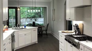 Een moderne keuken met witte kasten, een centraal eiland en een eetgedeelte met uitzicht op groen.
