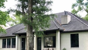 Een gelijkvloers huis met schuin dak, grote ramen en een voortuin met terrasmeubels.