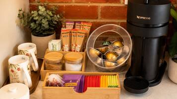 Una cocina con pared de ladrillo, una cafetera Nespresso, una tetera, una planta y varios objetos relacionados con el café.