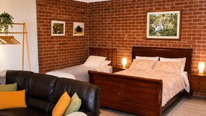 Une chambre avec un mur en briques, deux lits, une tête de lit en bois, un canapé en cuir et une petite table sur laquelle est posée une plante.