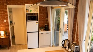 A compact kitchen with a refrigerator, microwave, and coffee maker. There is a wooden cutting board and a toaster on the counter. - Hilltop Haven Adelaide Hills Retreat Pet Friendly with Night and Day Yards (Mylor)
