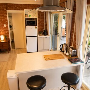 A compact kitchen with a refrigerator, microwave, and coffee maker. There is a wooden cutting board and a toaster on the counter. - Hilltop Haven Adelaide Hills Retreat Pet Friendly with Night and Day Yards (Mylor)