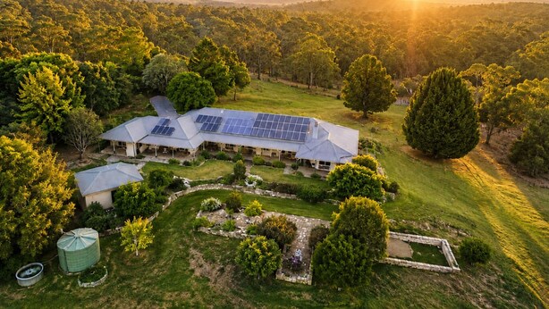 Une grande maison dotée de panneaux solaires, entourée d’une végétation luxuriante et d’arbres.