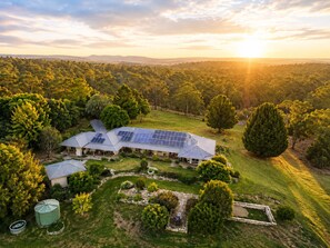 Une grande maison dotée de panneaux solaires, entourée d’une végétation luxuriante et d’arbres.