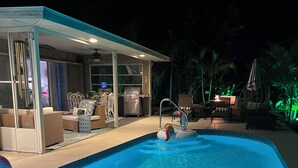 Ein Swimmingpool mit überdachter Sitzgruppe, Grill und Gartenmöbeln.