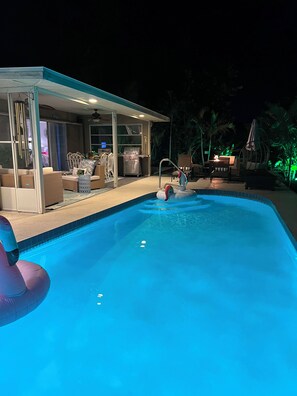 Ein Swimmingpool mit überdachter Sitzgruppe, Grill und Gartenmöbeln.