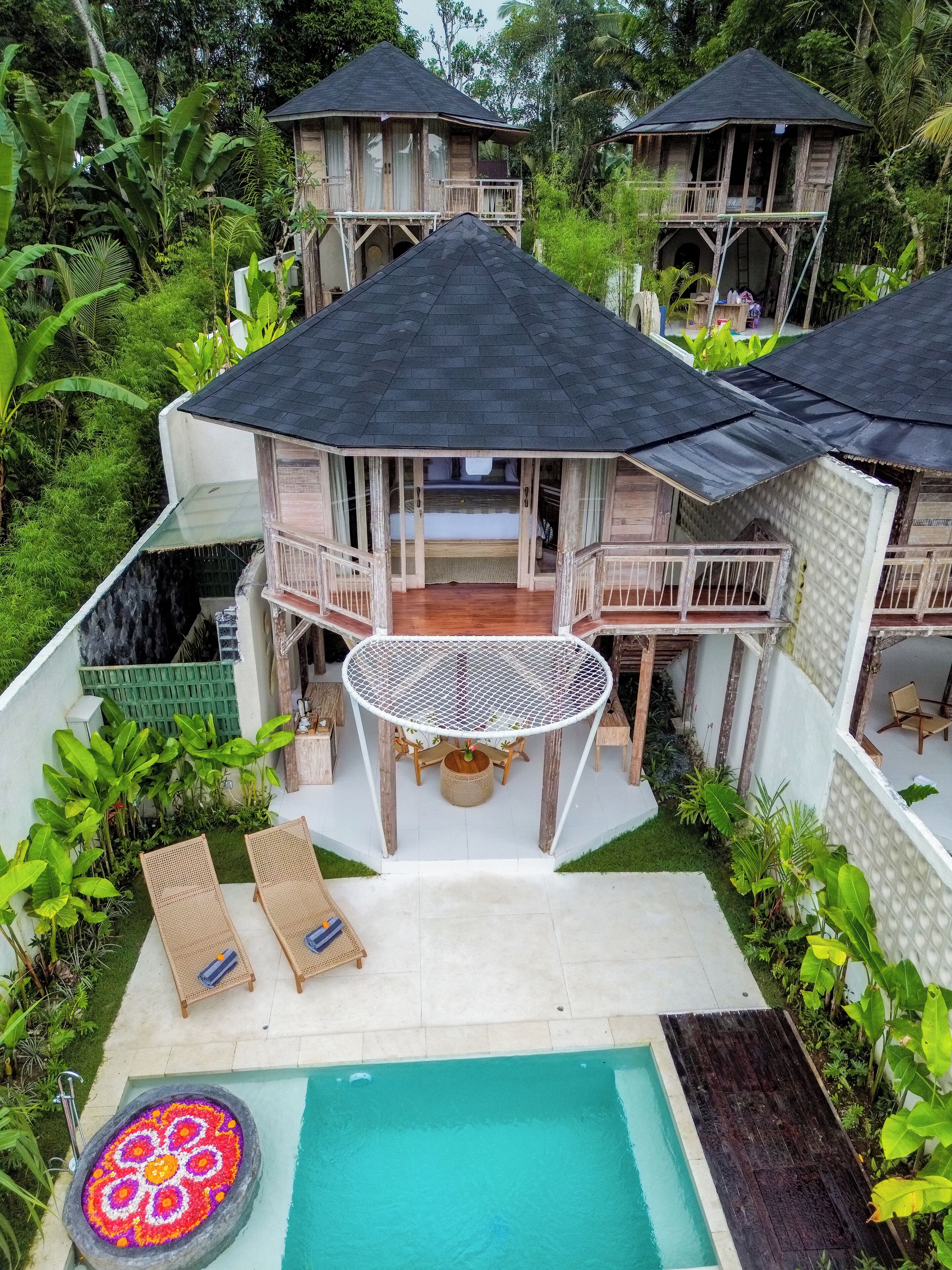 A resort with multiple wooden structures, a pool with a decorative flower pattern, and lush greenery.