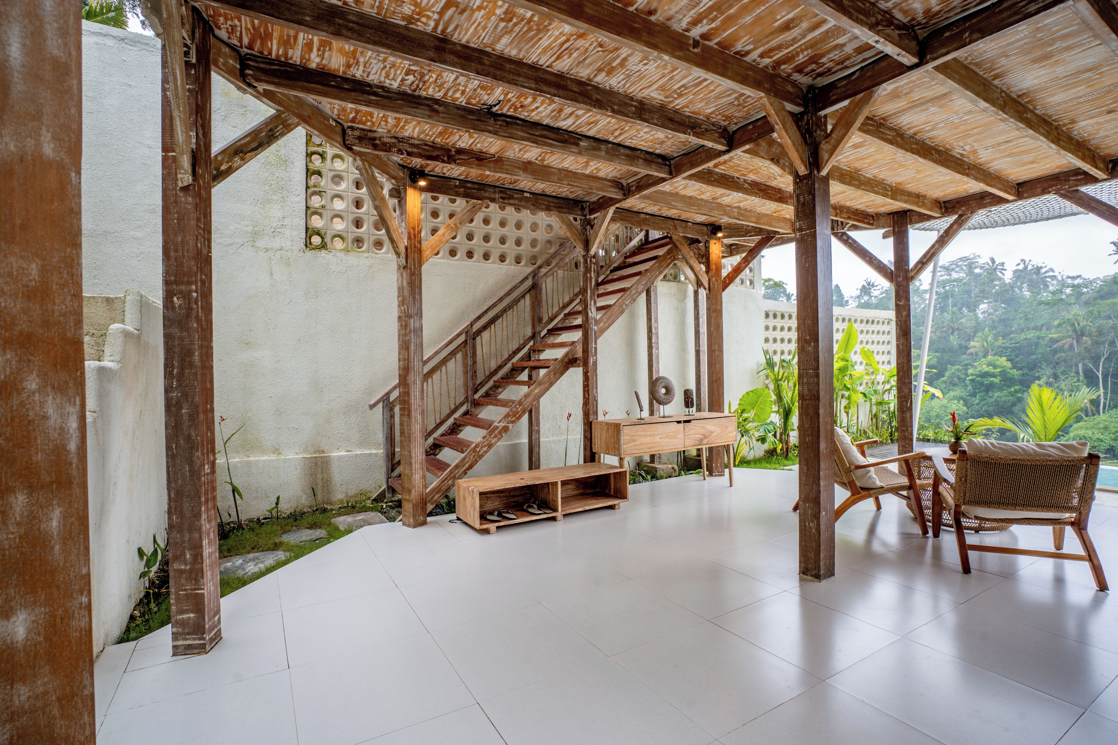 Un espace extérieur abrité, doté d’un escalier en bois, d’un banc et de deux fauteuils en osier.