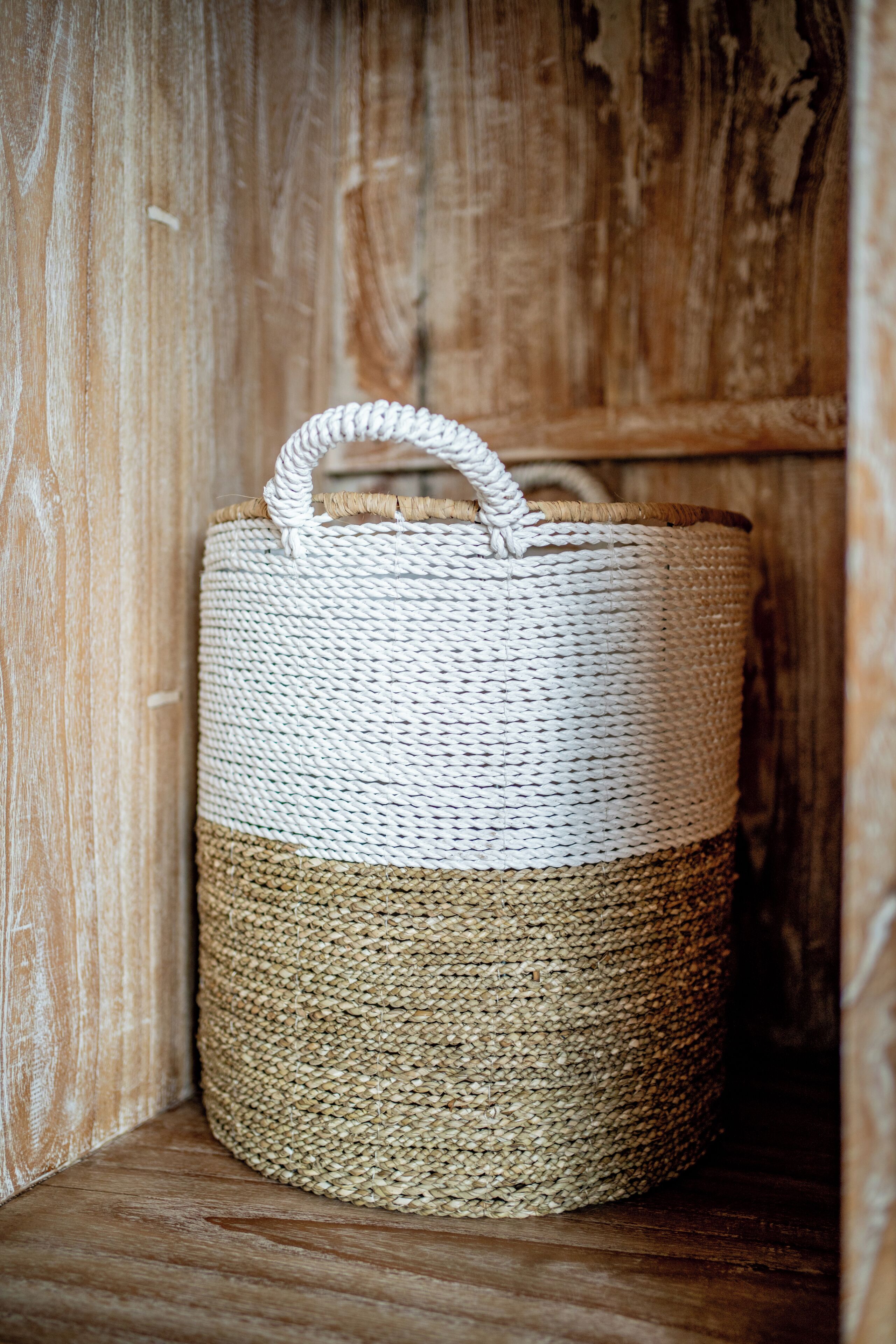 A woven basket with a handle, placed against a wooden background.